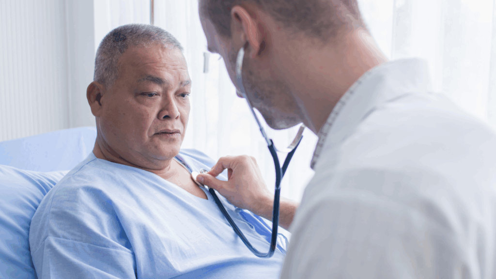 Hypertension: A doctor using a stethoscope to check the heartbeat of an older male patient lying in a hospital bed.