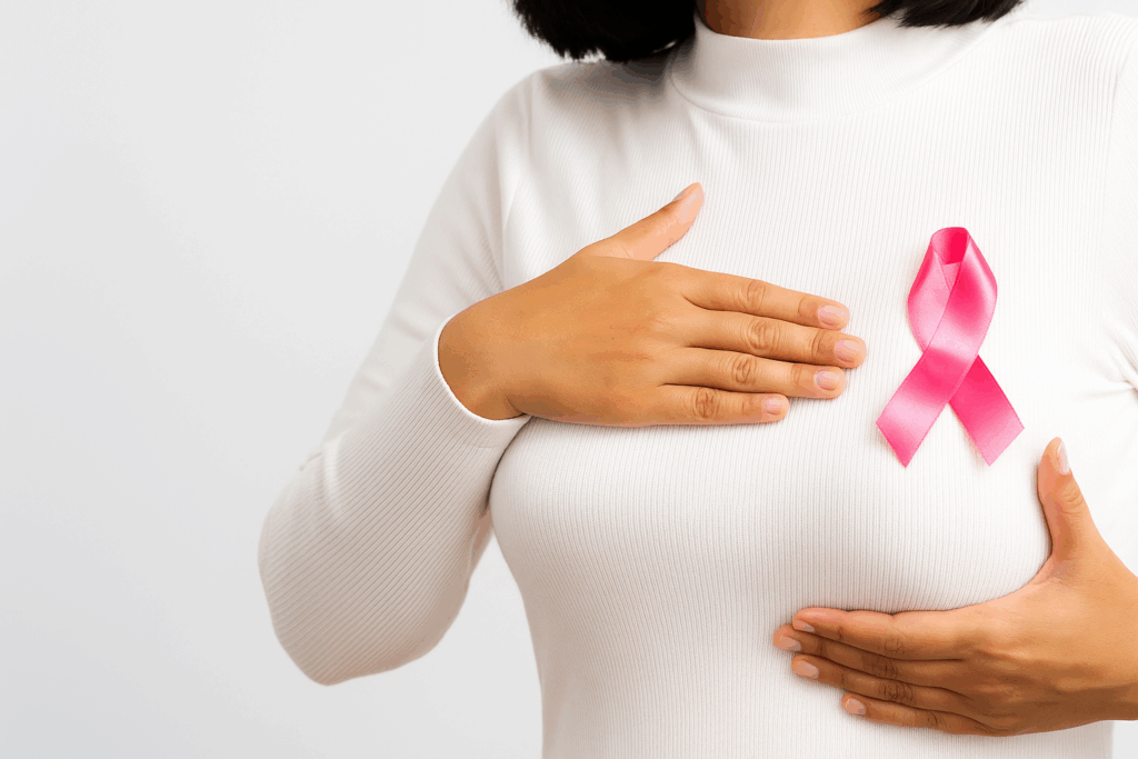 A woman with a pink breast cancer awareness ribbon pinned on her chest, holding her breasts with both hands as a gesture of support and awareness.