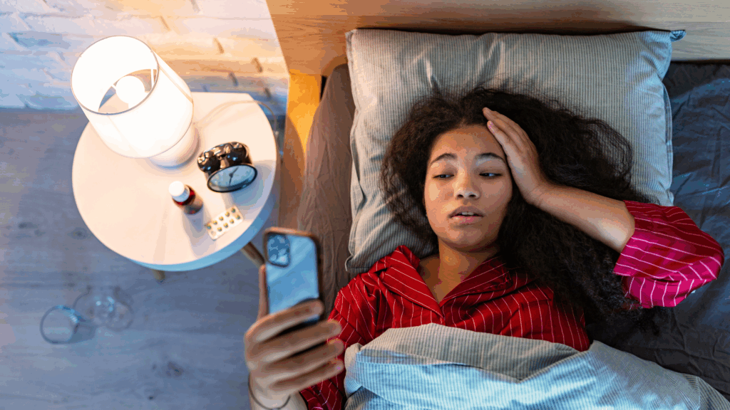 Woman lying in bed looking at her phone late at night, struggling with poor sleep and insomnia.